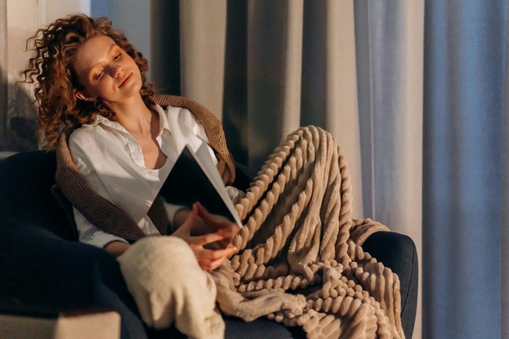 A woman with curly hair relaxing on a sofa, reading a book and enjoying a cozy atmosphere at home.